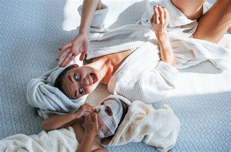 Mother And Daughter Have Spa Day With Beauty Masks On Faces Lying Down On Bed With Towels On