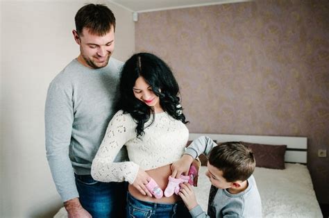 El Esposo La Esposa Embarazada Y El Hijo Miran Ropa De Bebé Para Recién Nacido En Casa Foto