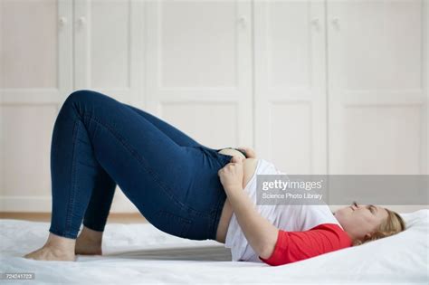 Young Woman Lying On Bed Trying To Button Jeans Photo Getty Images