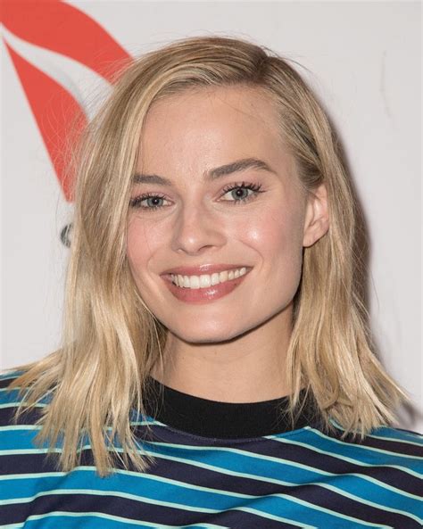 A Woman With Blonde Hair And Blue Striped Shirt Smiles At The Camera While Standing In Front Of