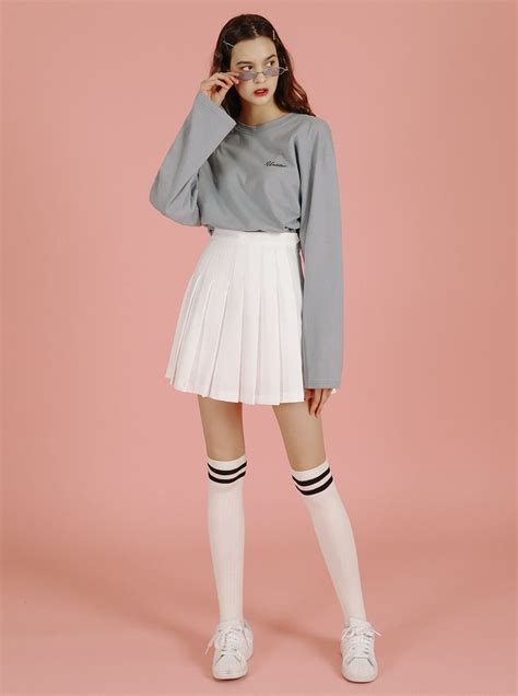 A Woman In A Gray Sweater And White Pleated Skirt Is Posing For The Camera