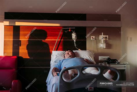 Patient Lying In Hospital Bed With Silhouette Of A Woman Behind Curtain