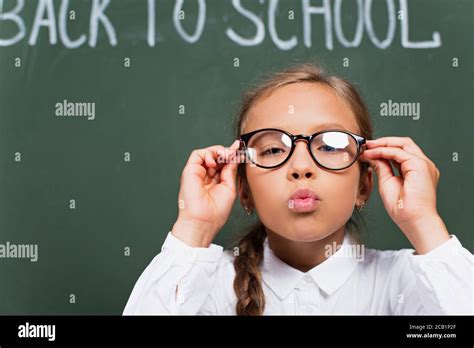 Selective Focus Of Cute Schoolgirl Touching Eyeglasses And Blowing Air