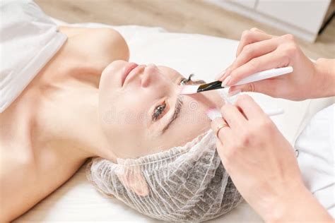 Beautician Rubbing Cream With Brushes Into Female Face Skin For Rejuvenation Cosmetic Procedure