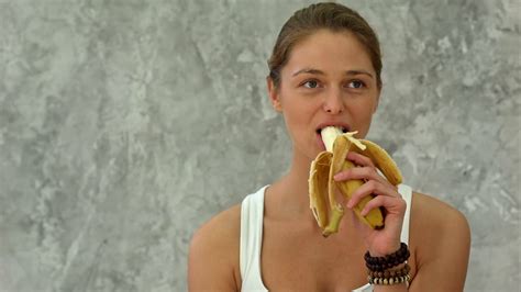Young Woman Holding Banana Eating It Looking At Camera Stock Video