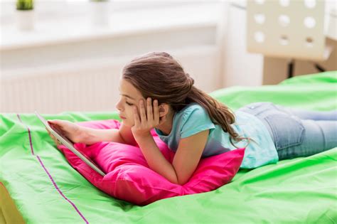 Bored Girl With Tablet Pc Lying In Bed At Home School Mum