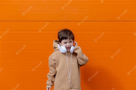 Un Niño Escucha Música Con Auriculares En El Fondo De Una Pared Naranja