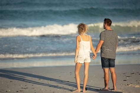 couple debout ensemble main dans la main sur la plage photo gratuite