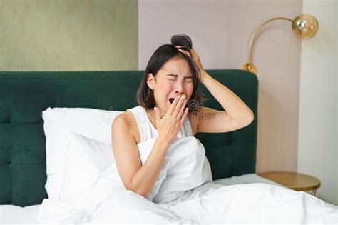 Woman Waking Up In Bed Yawning And Grimacing Early Morning After Sleep Sitting In Bedroom