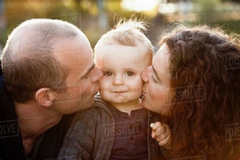 Parents Kissing Babys Cheeks Outdoors Stock Photo Dissolve