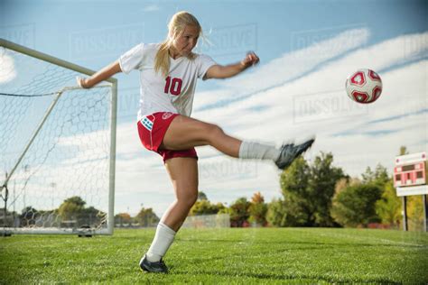 Low Angle View Of Athlete Kicking Soccer Ball On Field Under Blue Sky On Sunny Day Stock Photo