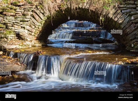 Waterfall Flowing Under An Old Arch Bridge Stock Photo Alamy