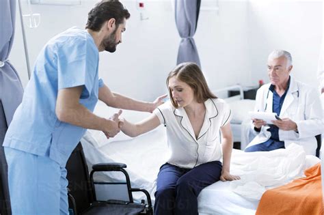 Doctor Helping Patient Out Of Hospital Bed Lizenzfreies Stockfoto