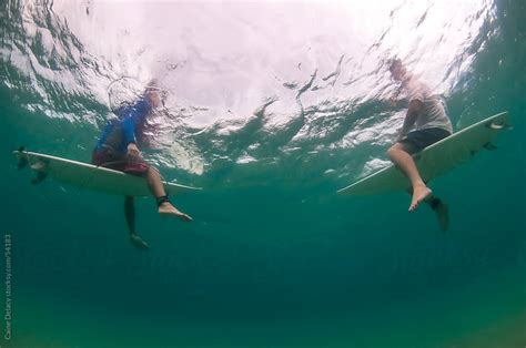 Sitting On Surf Boards In The Water Shot From Underwater Looking Up