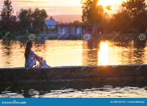 Back View Of Lonely Young Woman Sitting Alone On Lake Shore Enjoying