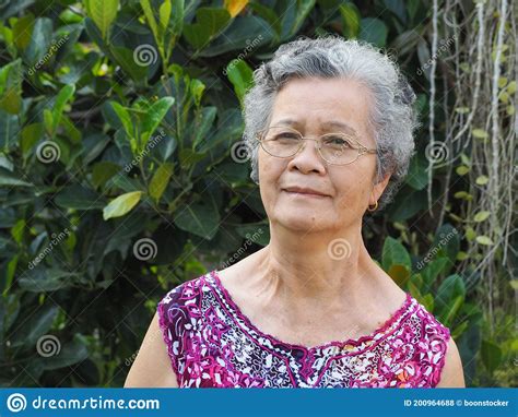 Senior Woman With Short White Hair Smiling And Looking At Camera While Standing In A Garden