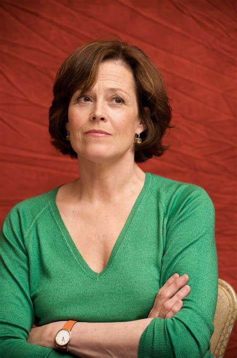 A Woman With Her Arms Crossed Sitting In Front Of A Red Wall Wearing A Green Sweater