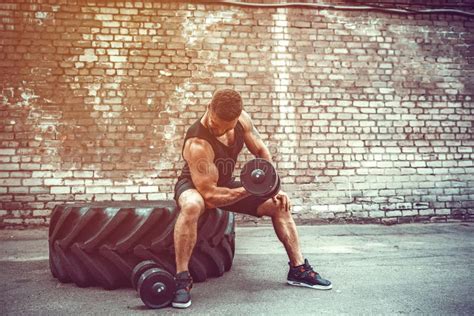 Muscular Guy Doing Exercises With Dumbbell Against A Brick Wall Stock