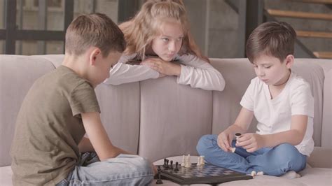 Older Sister And Two Younger Brothers Playing Chess Sitting On The