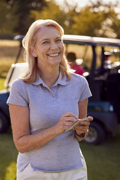 portrait of smiling mature female golfer standing by buggy on golf course with score card stock