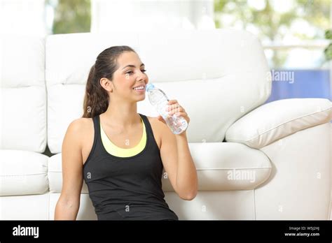 Happy Woman Drinking Bottled Water Sitting On The Floor At Home After
