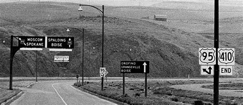 Black And White Photograph Of Highway Signs On The Side Of A Road In
