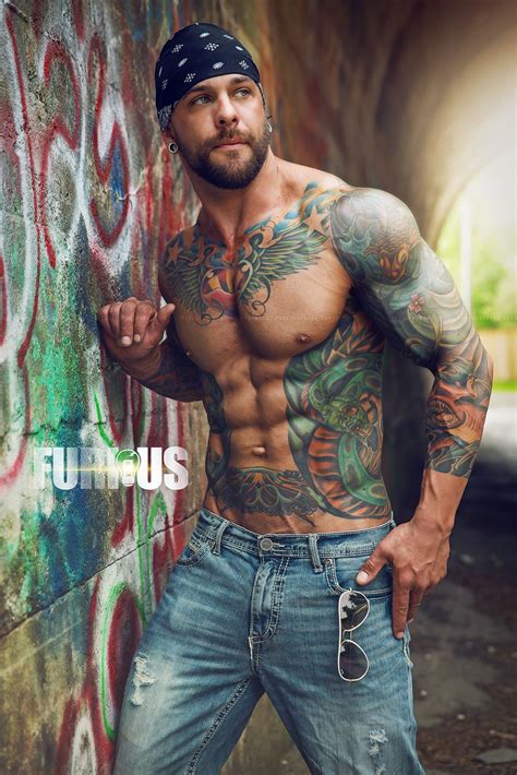 A Man With Tattoos Standing Next To A Wall