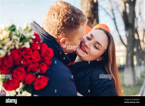 Valentines Day Date Man Kissing Girlfriend On Cheek Outdoors Ting Bouquet Of Red Roses