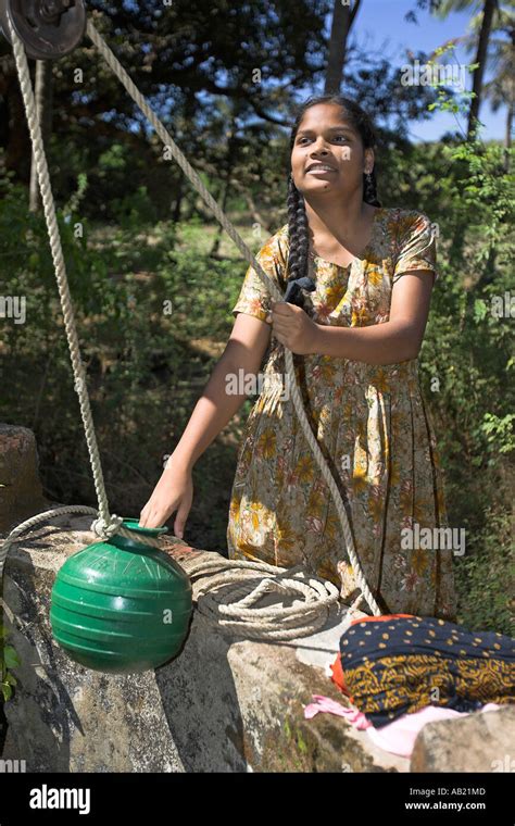 Young Woman Draws Water From Well By Hand With Green Pot On Traditional Rope Pulley Mandrem