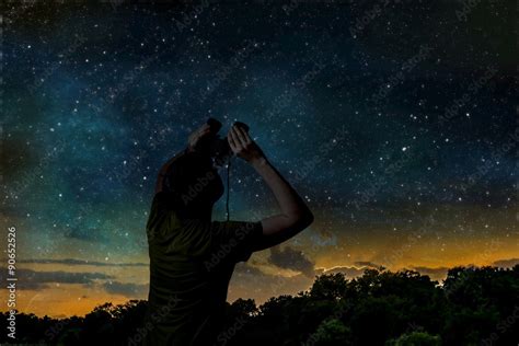 Silhouette Of Adult Man Is Observing Stars On Night Sky With Binoculars