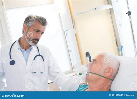 Doctor At Hospital Bedroom With Sick Patient Lying In Bed Stock Photo