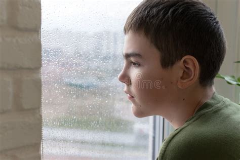 Portrait Of A Sad Boy Looking Out The Window In Rainy Weather