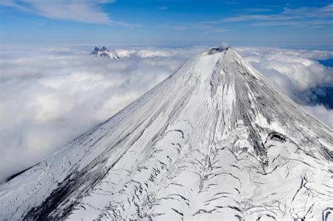 An Aerial View Of A Snow Covered Mountain Peak In The Sky With Clouds