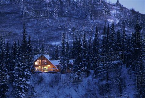 Home Cabin In Snow Covered Forest Lights On Dusk