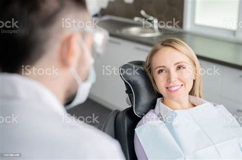 Happy Young Blonde Female Patient Looking At Her Dentist With Healthy