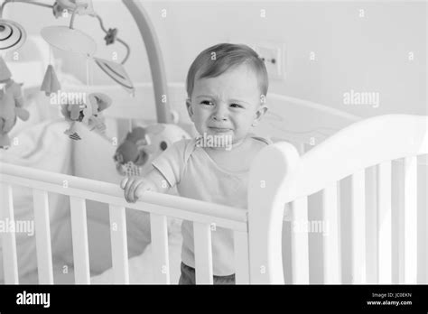 Black And White Portrait Of Baby Boy Standing In Crib And Crying Stock