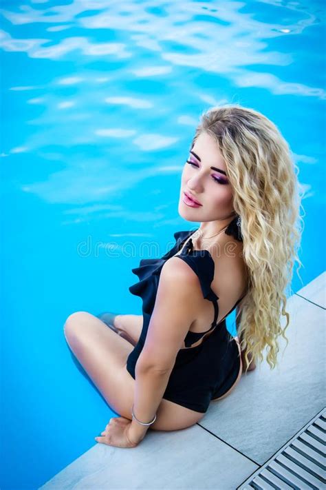 schöne junge blondine sitzt am rand des pools sinnliche sexy frau auf dem hintergrund des pools