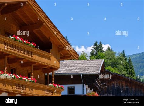 Traditional Wooden Austrian House With Red And White Flowers On Balcony