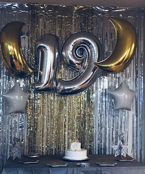A Table Topped With A Cake Covered In Gold Foil Balloons Next To A