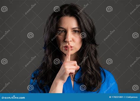Serious Woman With Long Hair Holding Finger On Her Lips Over Grey