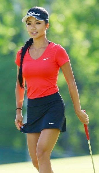 A Woman In A Red Shirt And Black Skirt Holding A Golf Club While Walking Across A Green Field