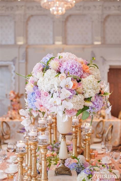 A Table Topped With Lots Of Gold Vases Filled With Purple And White
