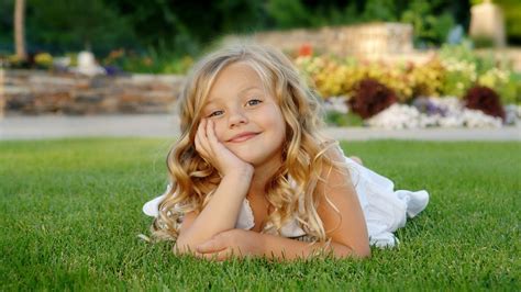 Smiley Cute Little Girl Is Lying Down On Green Grass