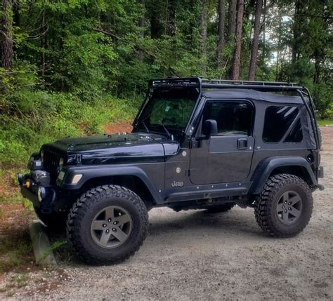 A Black Jeep Parked On Top Of A Dirt Road In Front Of Some Green Trees
