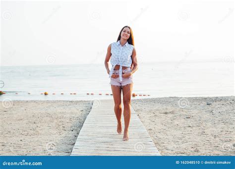 Beautiful Tanned Woman With Long Hair Walks On The Beach By The Sea