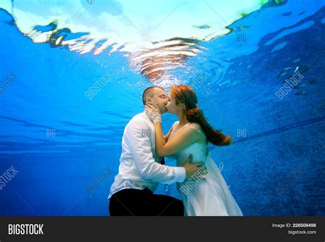 The Bride And Groom In Wedding Dresses Kissing Underwater In The Swimming Pool Portrait