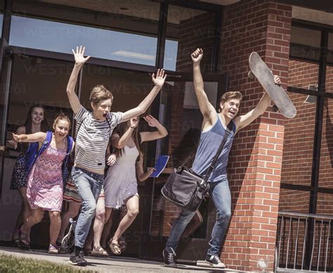 Male And Female High School Students Running Out Of High School Stock Photo