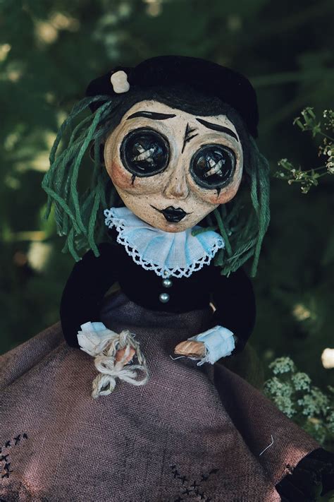 A Doll With Green Hair And Big Eyes Sitting In Front Of A Tree Wearing A Dress