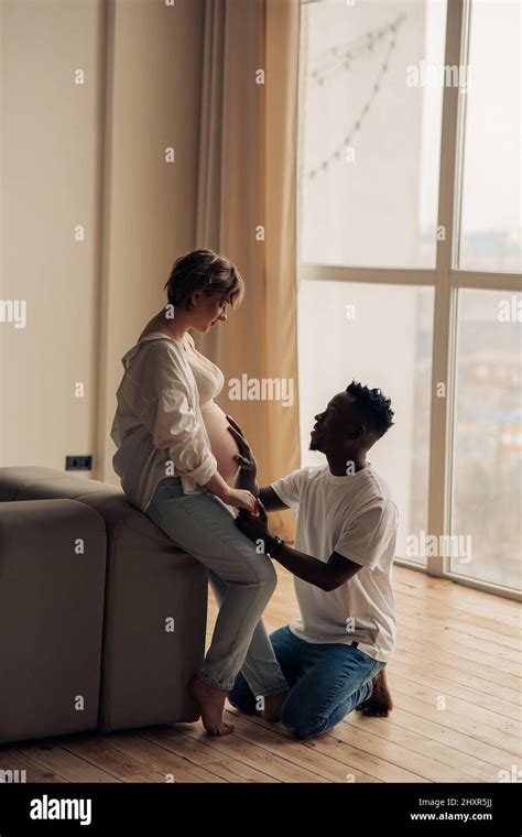 Young Happy African Man Kneels Before His Caucasian Pregnant Woman And