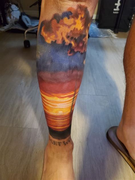 A Man S Leg With A Sunset And Clouds Tattoo On It